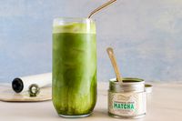 A glass of Matcha Bar Premium Blend next to the container