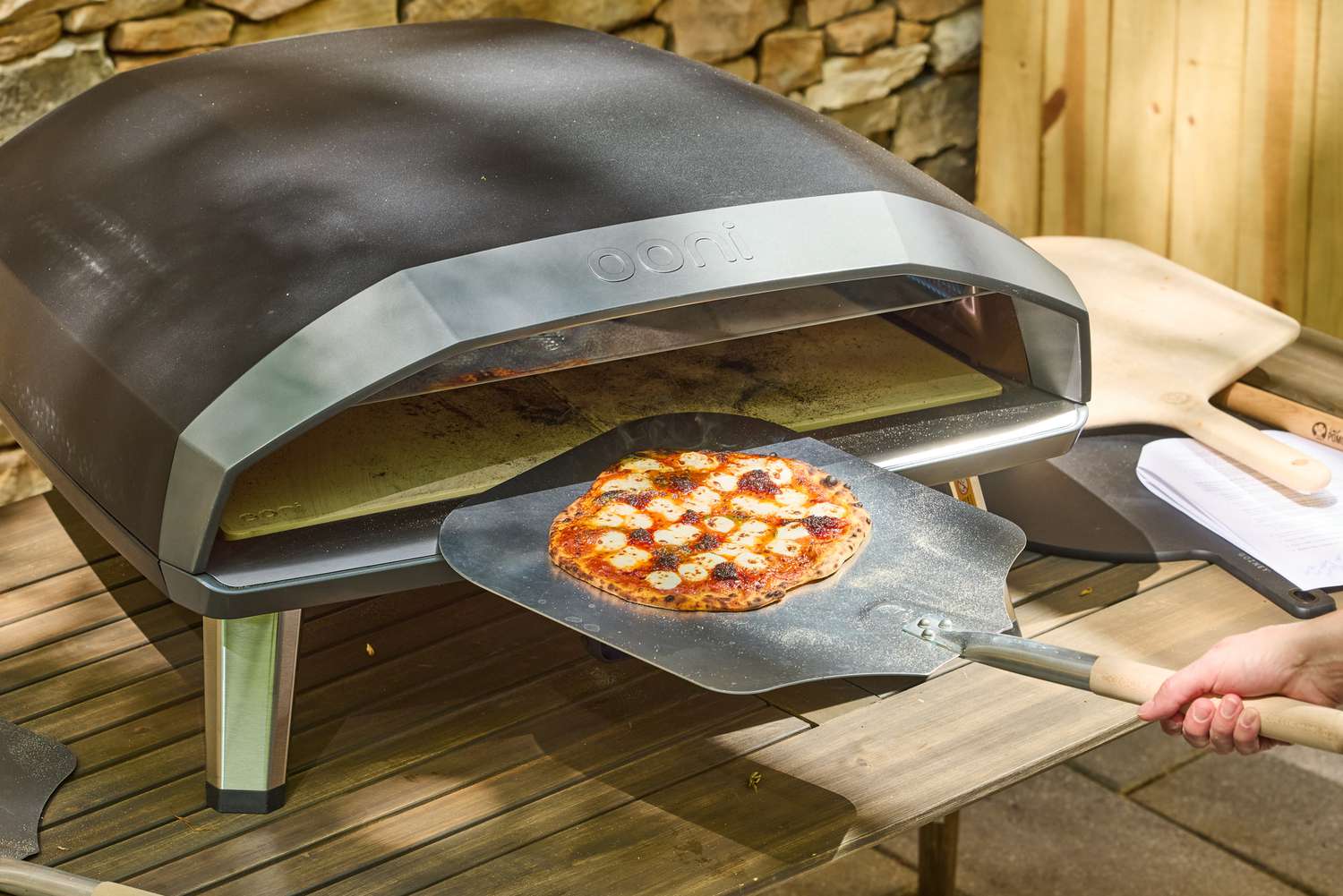 A person removes a pizza from the Ooni Koda 2 Max Gas Powered Pizza Oven