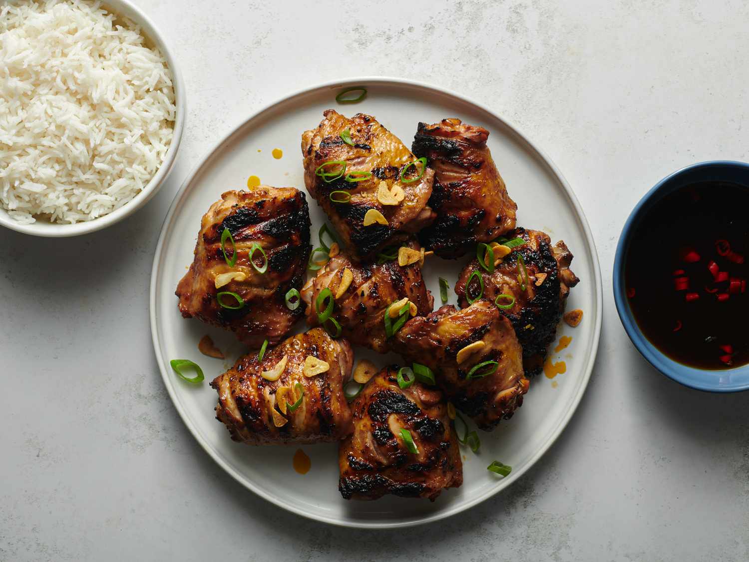 Overhead view of finished chicken inasal on a plate next to dipping sauce and white rice