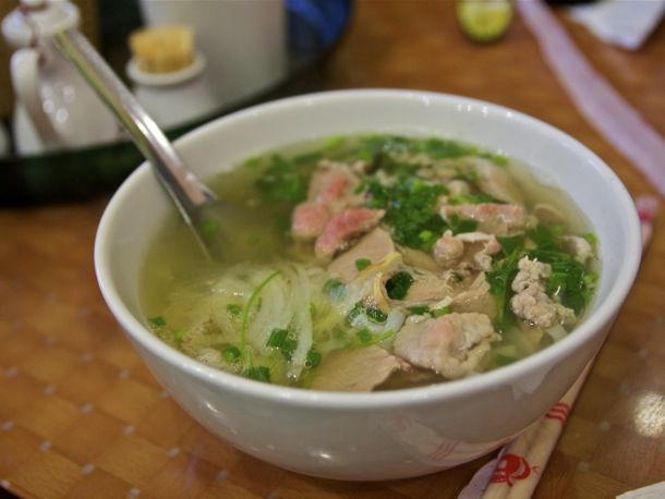 A white bowl of Phở with meat and onions in the broth 