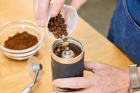 A person pours coffee beans into the 1Zpresso J Manual Coffee Grinder