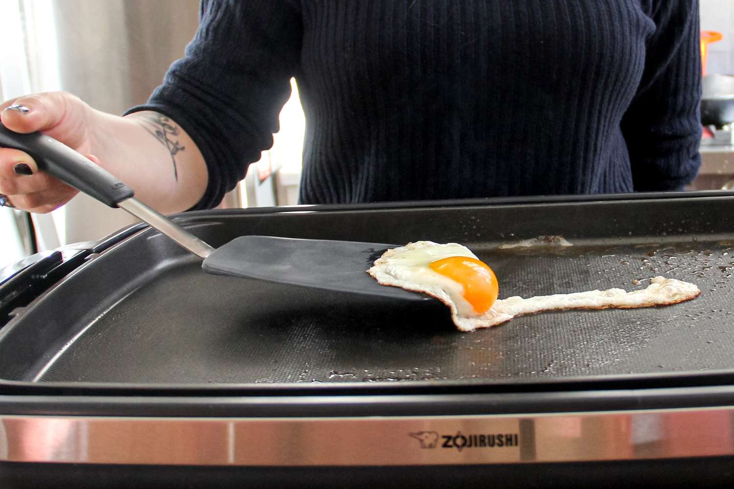 A person lifting a fried egg from a nonstick griddle with a food turner