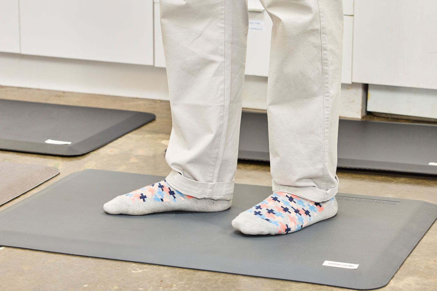 A person stands on the WellnessMats Original Anti-Fatigue Floor Mat in socks