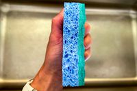 An O-Cedar Scrunge being held over a stainless steel sink