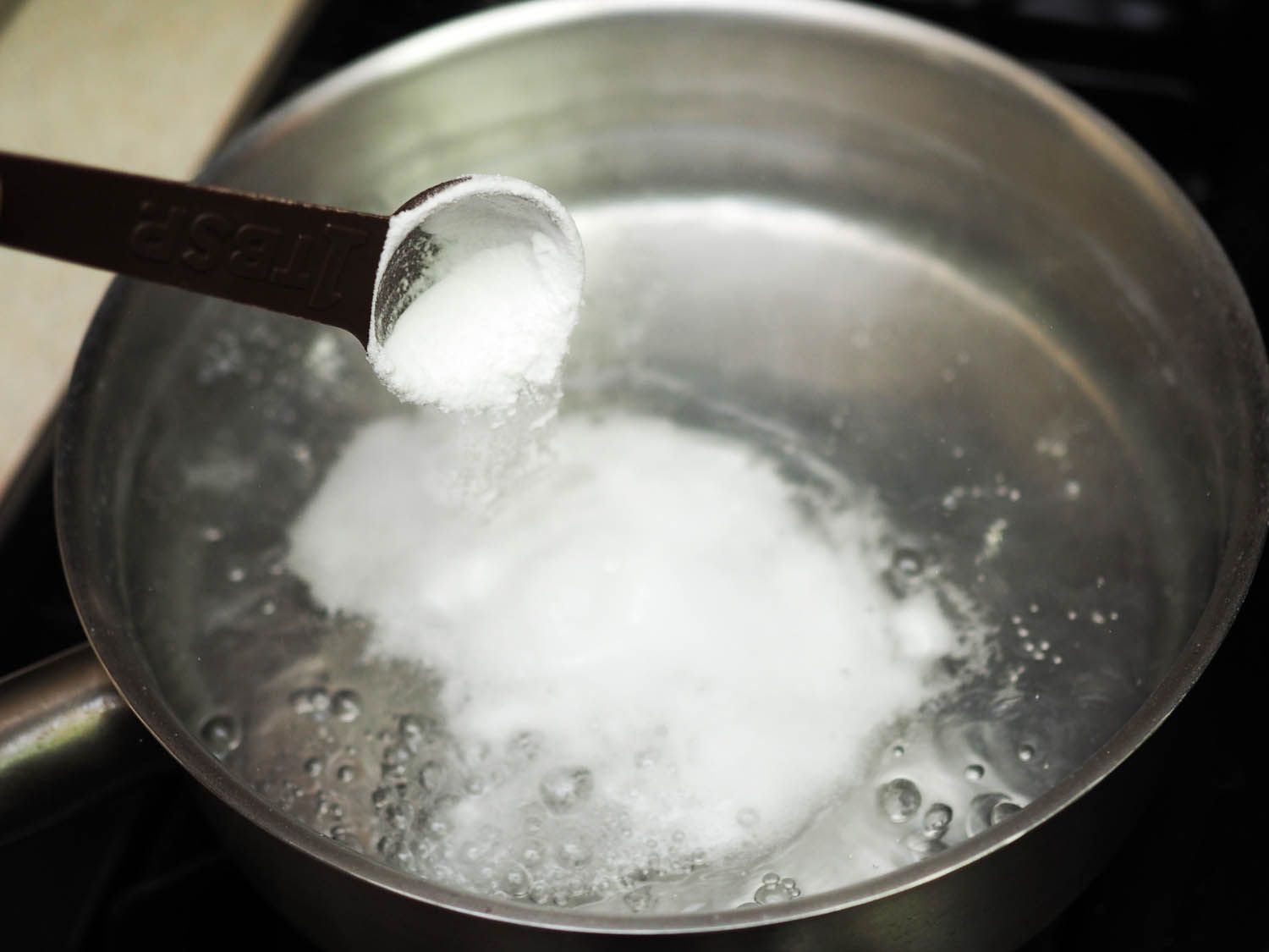 Adding baking soda to a pot of boiling water. 