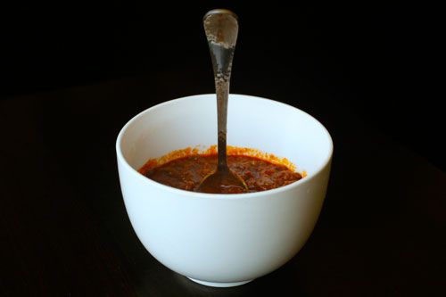 Side view of a bowl of chili with a submerged spoon standing in its center, at a perpendicular angle to the chili's surface.