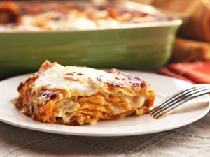 Cross-section view of a wedge of squash lasagna, with the full lasagna pan out of focus just behind it.