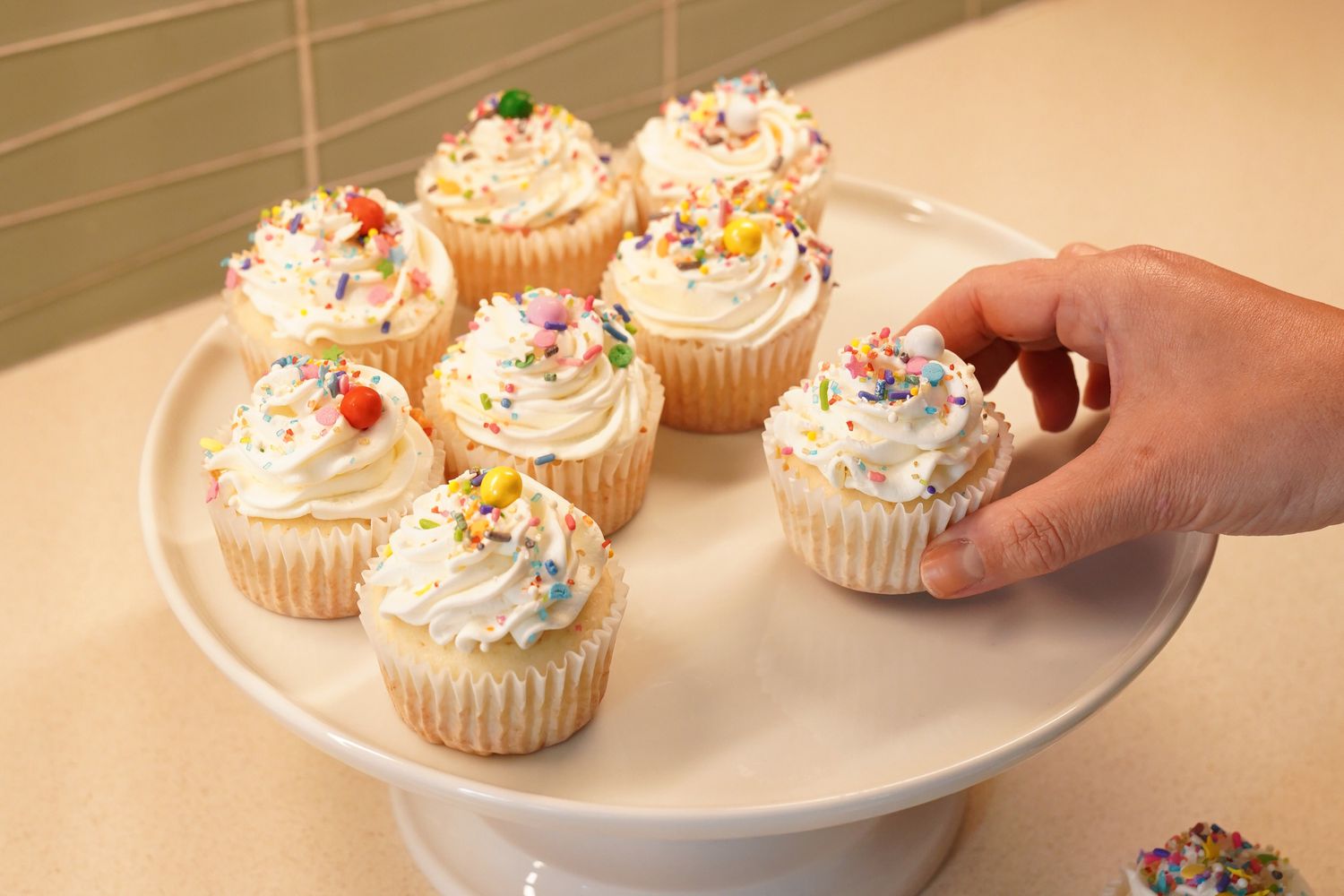 A collection of frosted cupcakes sits on a white ceramic cake stand.