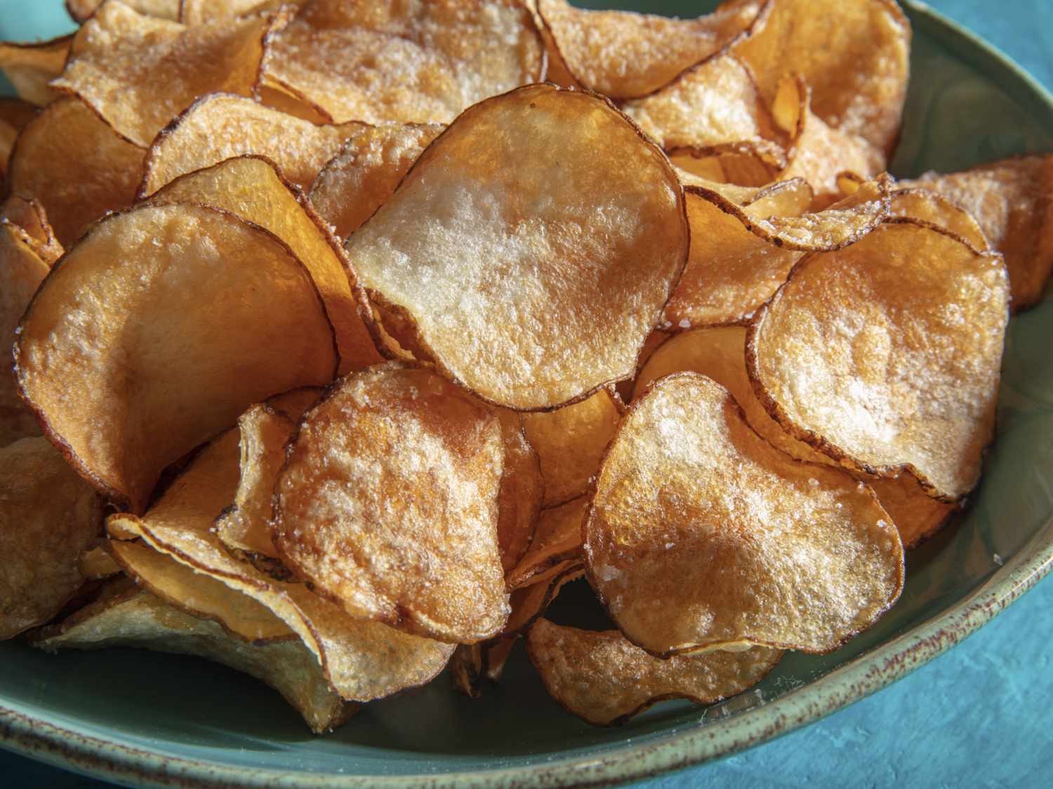 Potato chips piled in a ceramic bowl, showing off the brown and crispy color and texture of the chips.