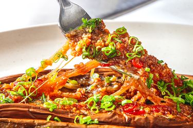 A fork lifting a piece of Chinesestyle BBQ eggplant garnished with chopped green onions on a plate