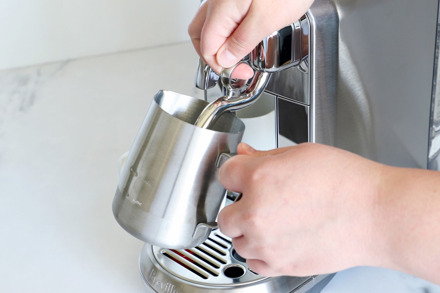 A person steaming milk using a metal pitcher and an espresso machine