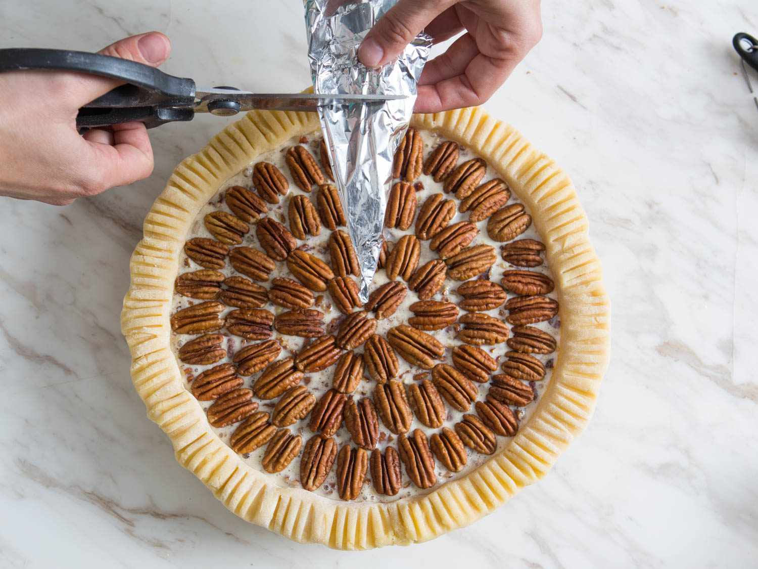 Cutting a folded triangle of aluminum foil to form a circular shield for the pecans.