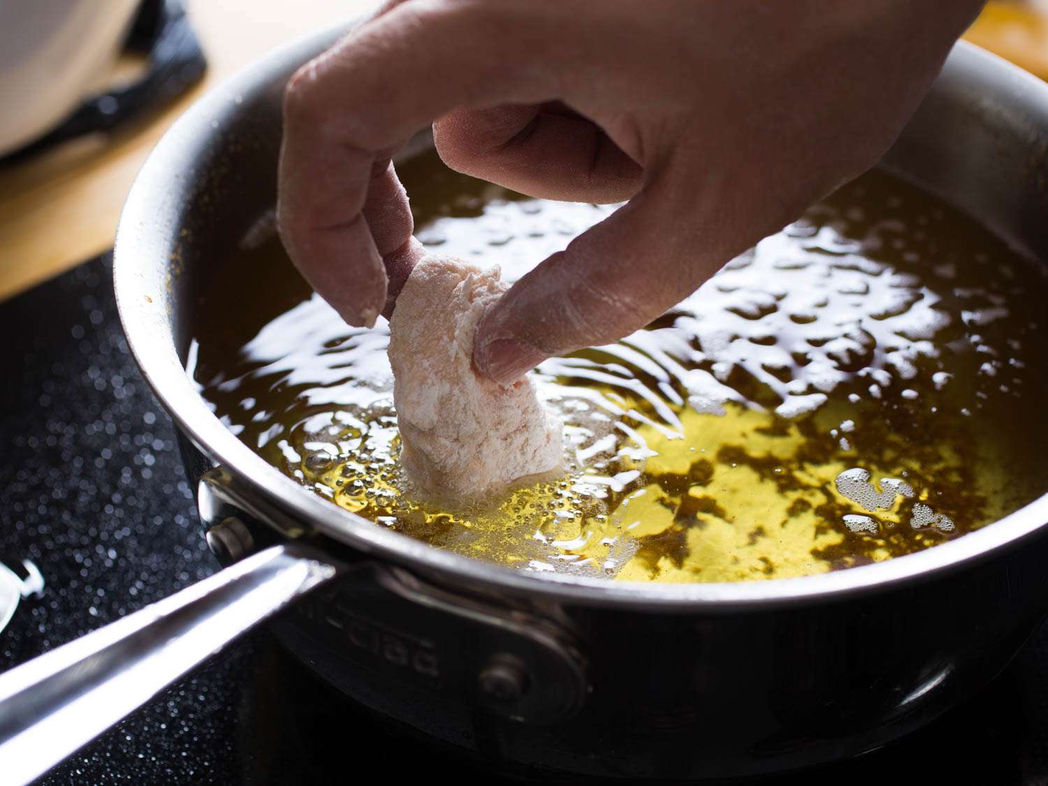 Lowering battered and flour coated fish into a pan of hot oil