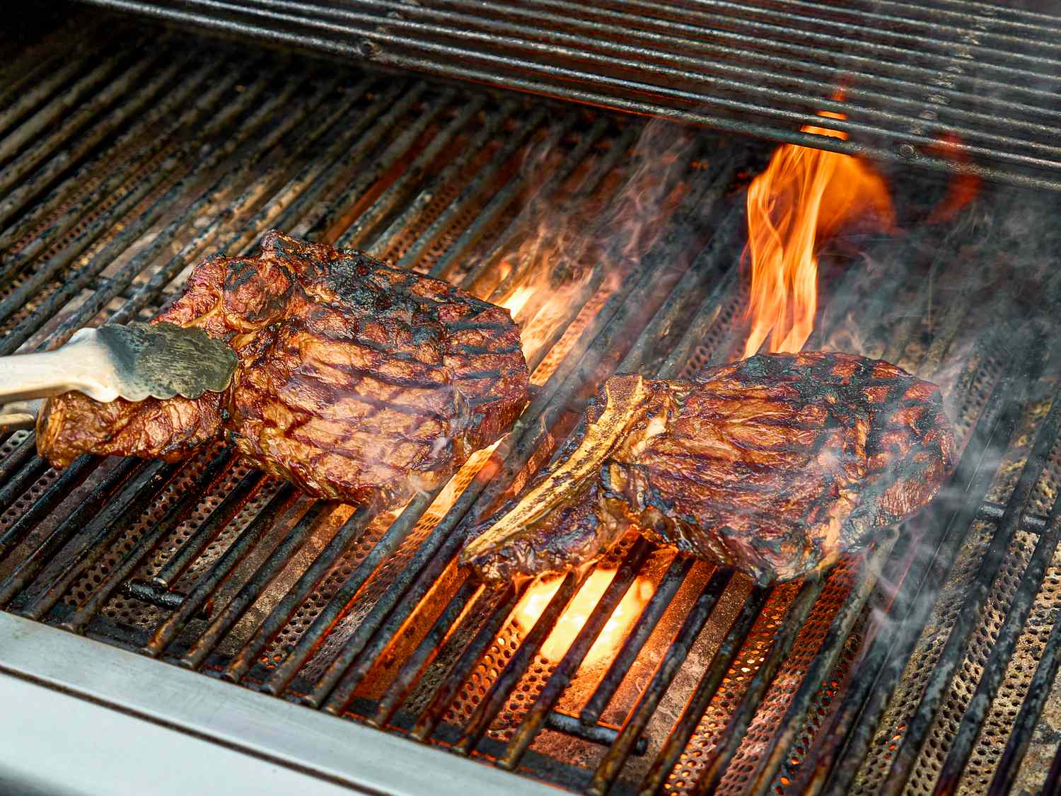 Two steaks cooking on a grill with flames visible underneath
