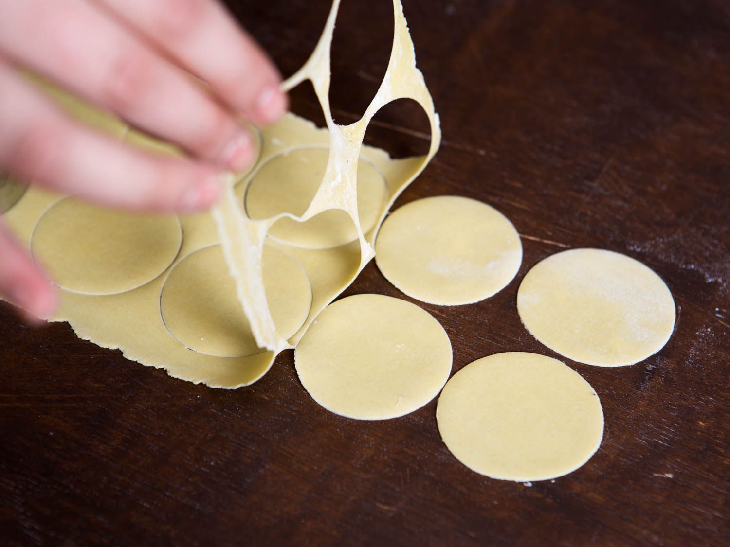 Lifting up the extra dough after cutting out circles for tortellini. 