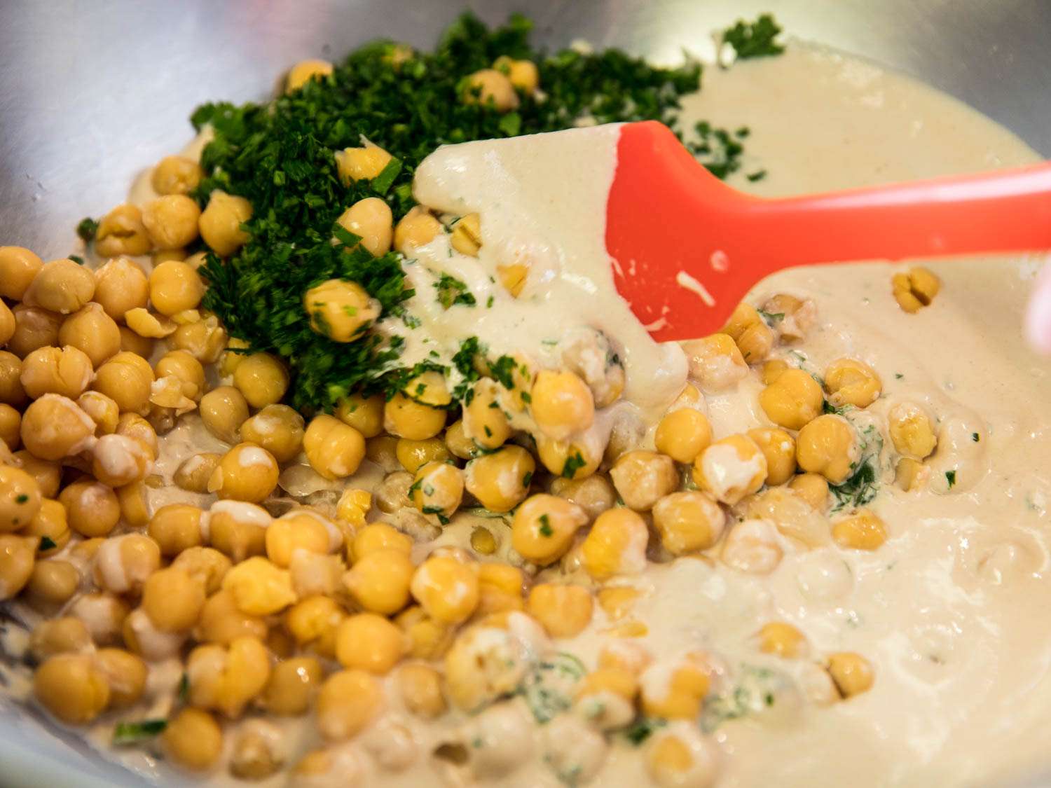 Folding together tahini hummus, chickpeas, and chopped parsley
