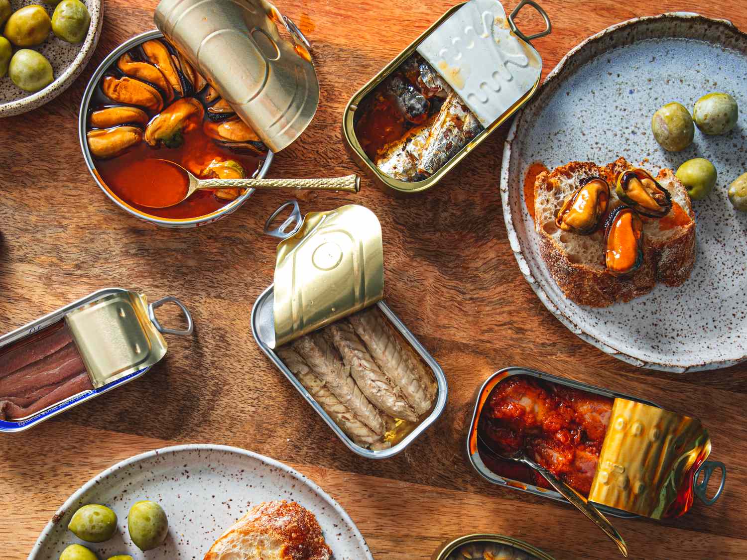 An arrangement of various open tins of fish displayed with accompaniments like olives and bread