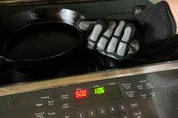 A person holds up a pan while wearing the Blackstone Griddle Gloves