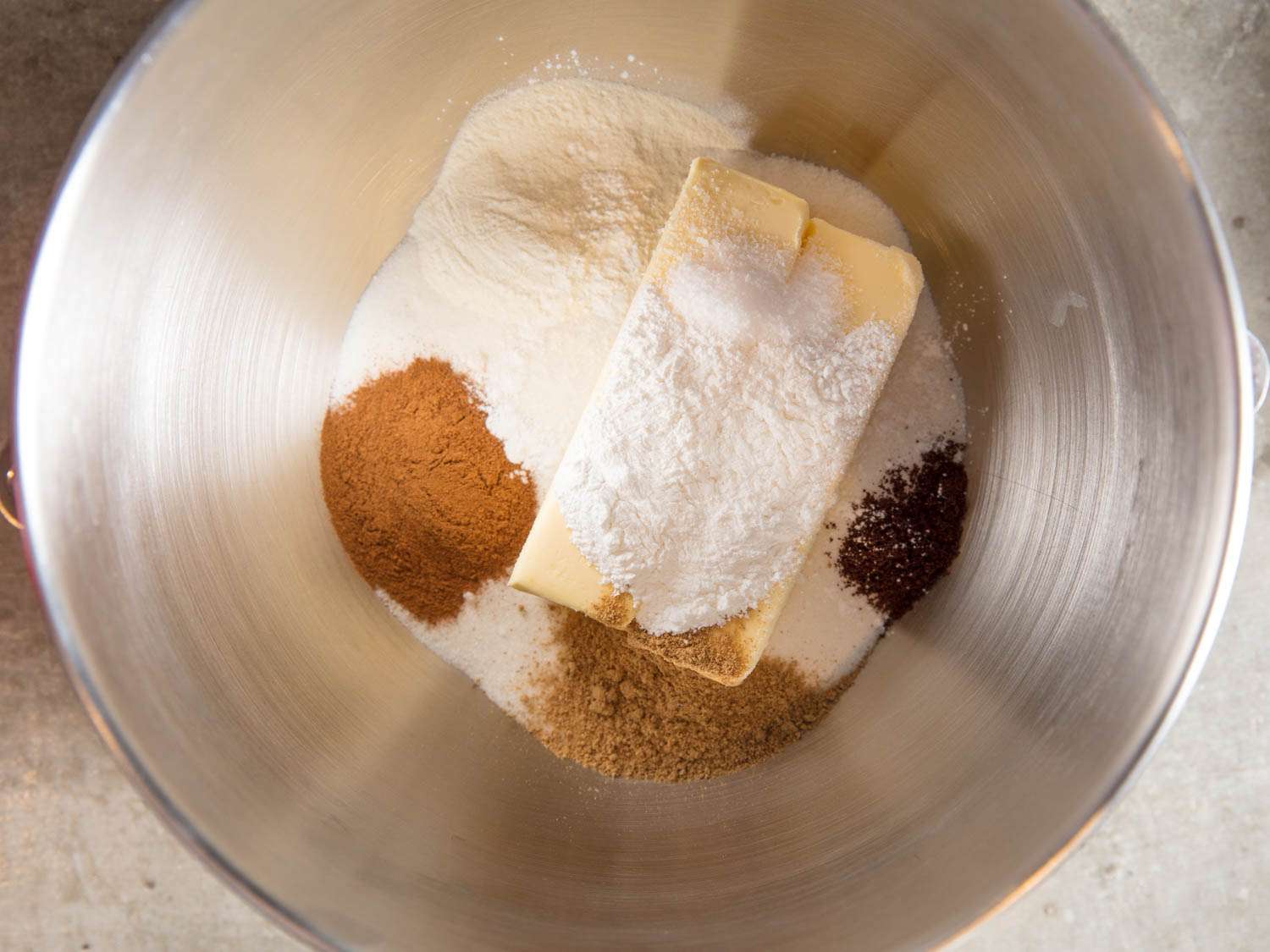 Overhead shot of sticks of butter, spices, sugar, baking powder, and potato flour in a metal bowl.