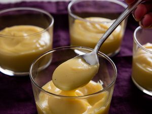 Four servings of butterscotch pudding. A spoonful of butterscotch pudding is held up to the camera.