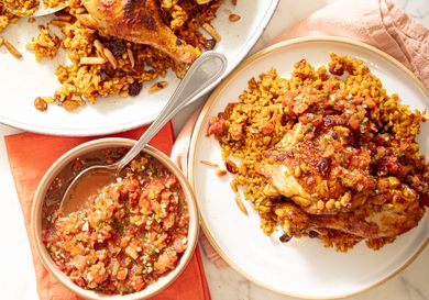 Plates of cooked chicken served with seasoned rice and a bowl of sauce on the side