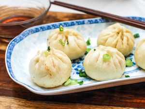 A small platter of sheng jian bao (pan-fried pork soup dumplings), sprinkled with sliced scallions.