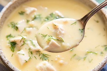 A bowl of soup with chunks of chicken herbs and a spoon