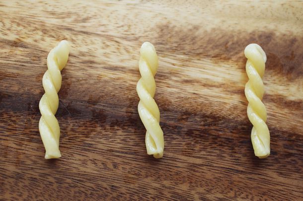 Three pieces of cooked gemelli pasta arranged in parallel on a wooden cutting board.