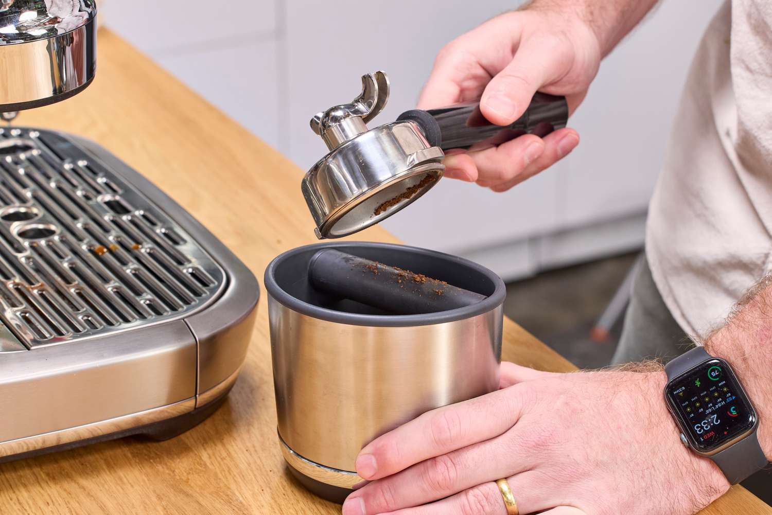 A person removes espresso grounds from the Breville The Oracle Dual Boiler Espresso Machine portafilter