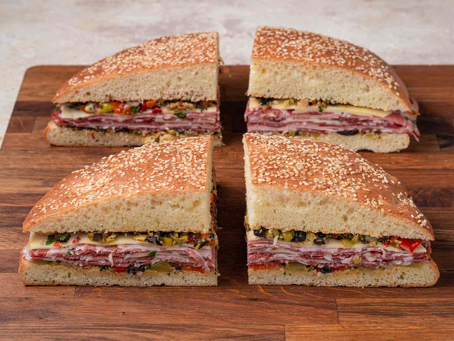 A muffuletta sandwich cut into quarters and displayed on a wooden cutting board.