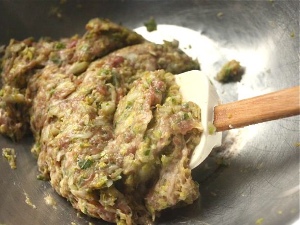 Dumpling filling inside of a metal mixing bowl, being stirred by a silicone spatula with a wooden handle.