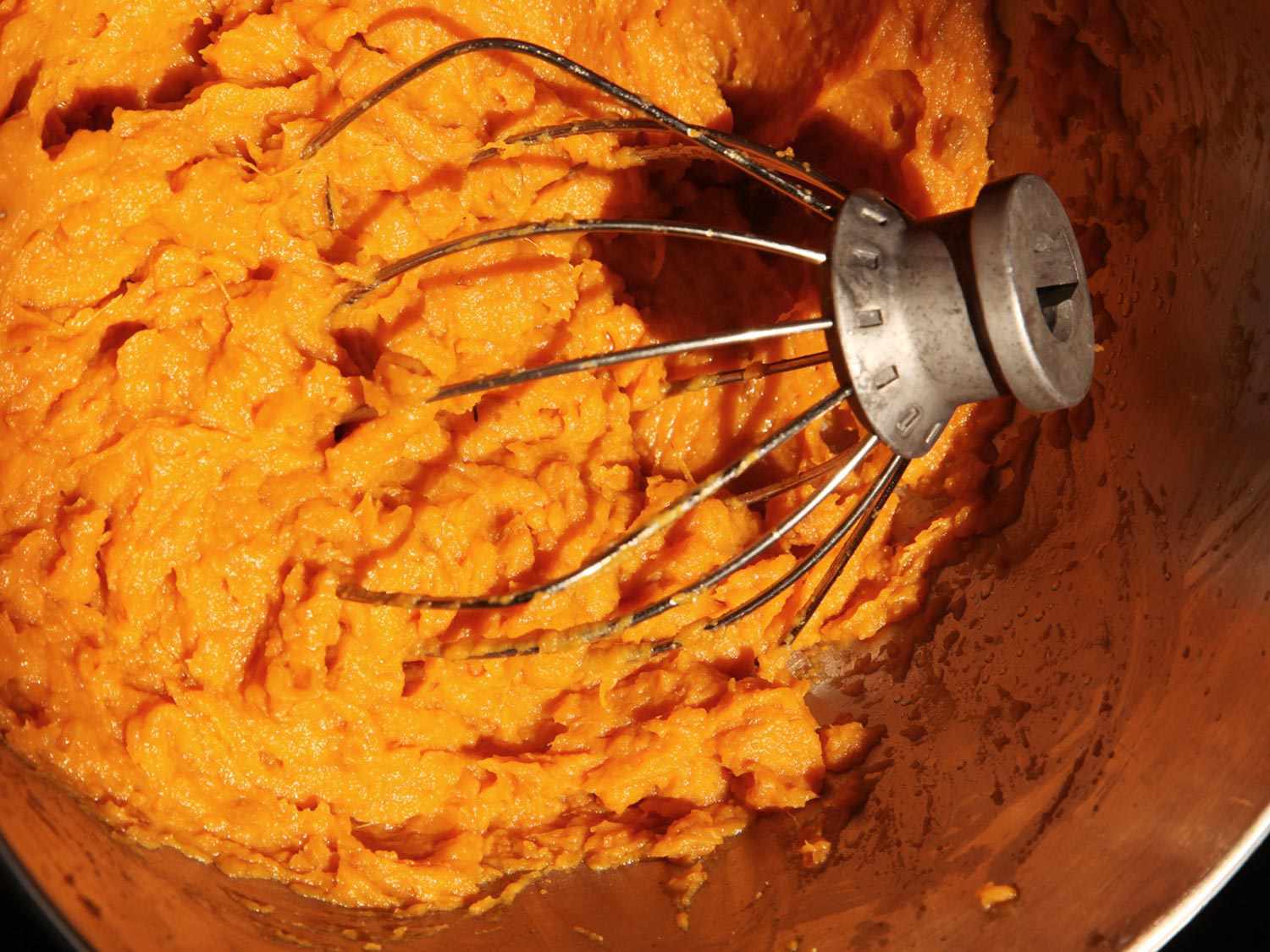 Whisk attachment in mixing bowl filled with creamy sweet potatoes 