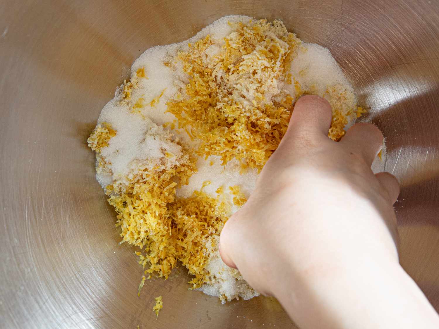 A hand mixing lemon zest and sugar in a bowl