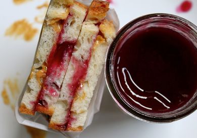 A peanut butter and jelly sandwich next to a jar of grape jam. 