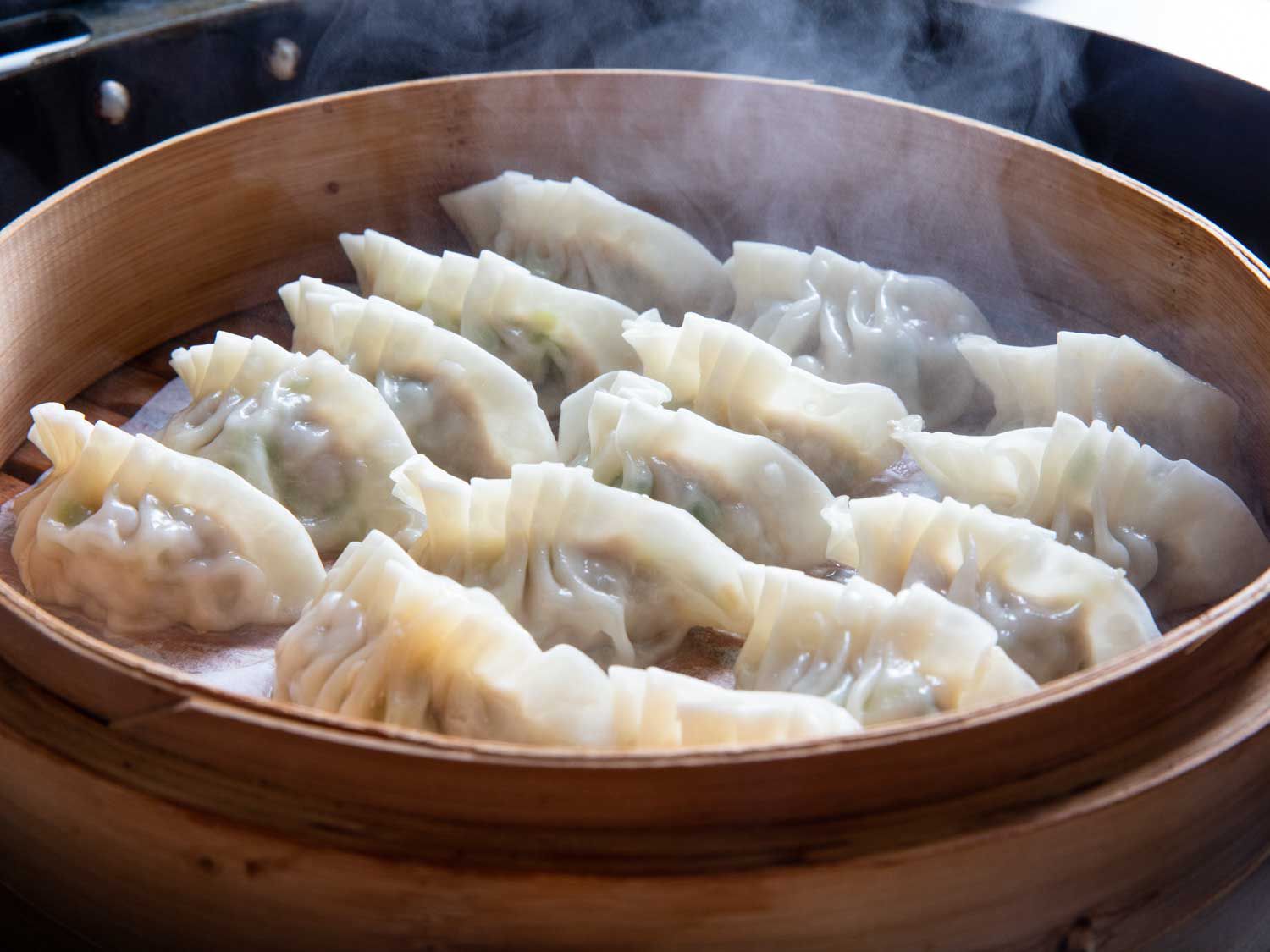 Homemade pork and scallion dumplings in a bamboo steamer. 