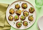 Platter of stuffed mushrooms garnished with parsley on a green surface. Serving plates, a green napkin and a green glass of sparkling water 