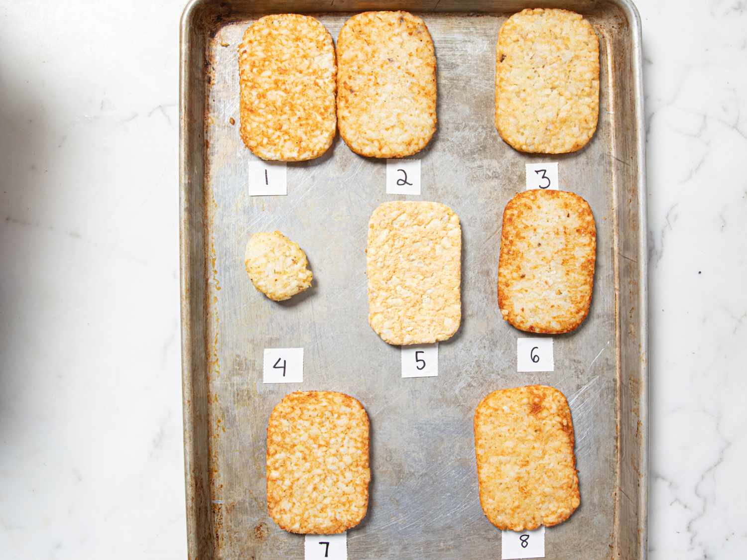 A tray with eight numbered hash browns arranged for a taste test