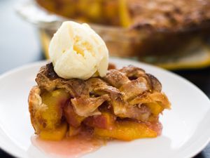 A slice of classic peach pie, served with a scoop of ice cream perched on top.