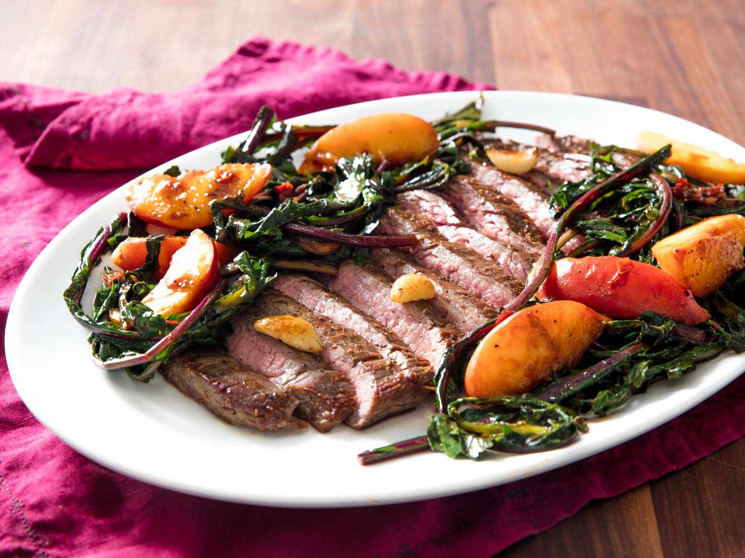 A platter of sliced seared flank steak with peaches and dandelion greens 