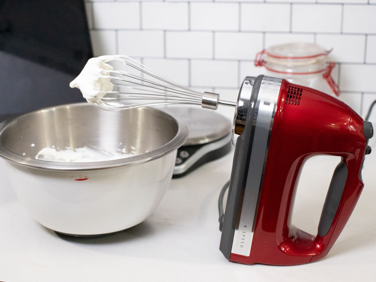 a hand mixer with its whisk attached and a bowl of whipped cream beside it