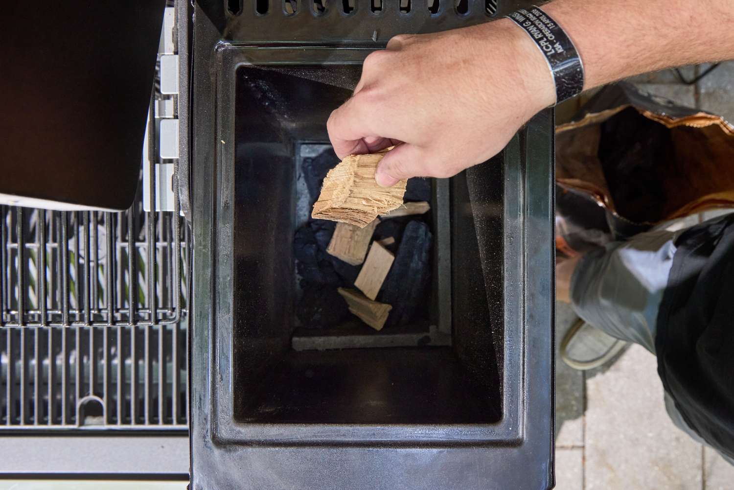 A person places wood chips into the Masterbuilt Gravity Series 1150 Digital Charcoal Grill and Smoker