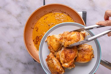 A plate with cooked chicken thighs being held above a copper pan
