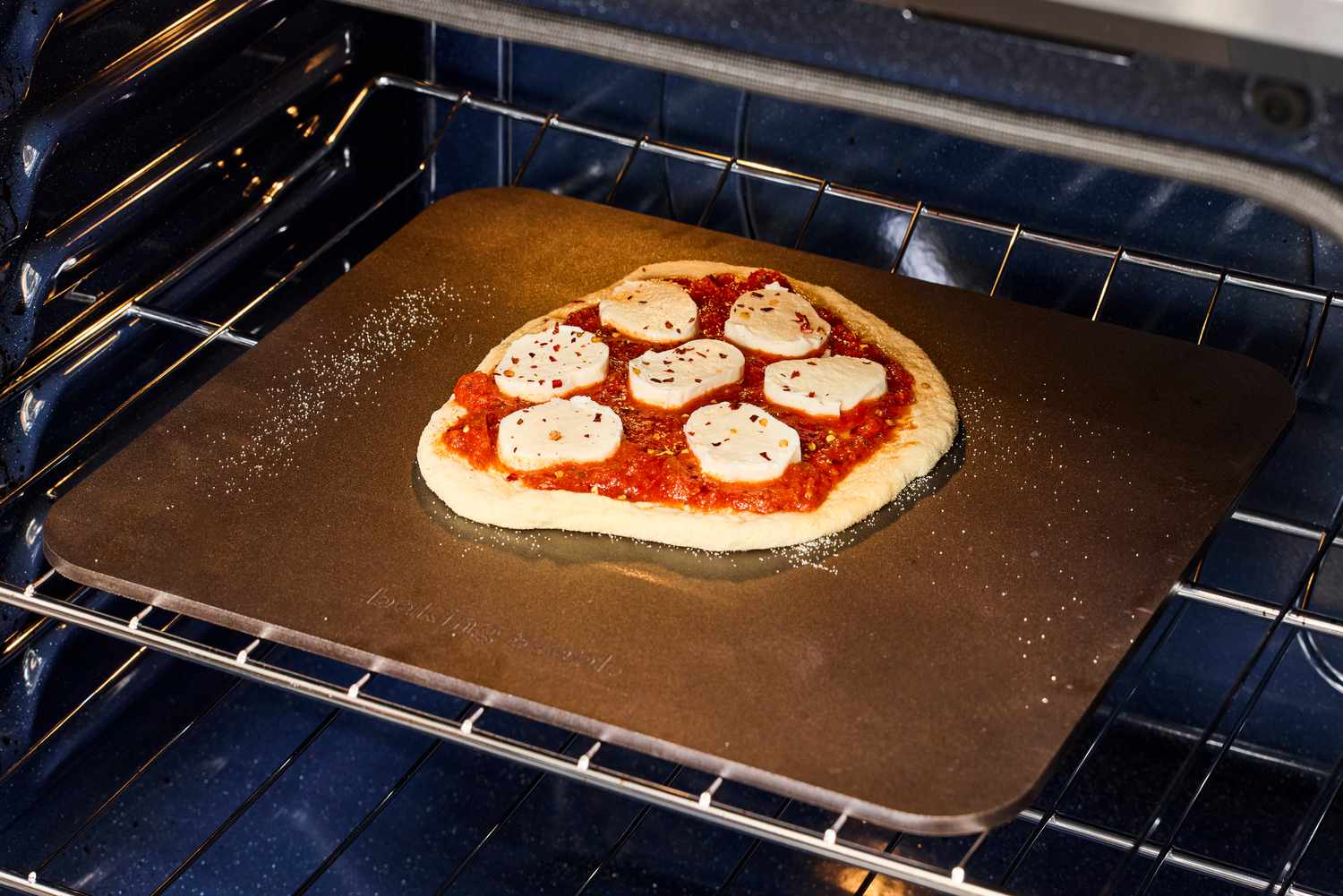 A pizza topped with mozzarella cheese and tomato sauce on a baking steel in the oven.