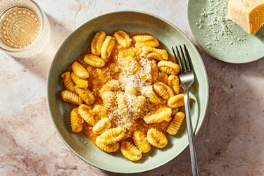 Fresh Cavatelli on a green bowl with a fork, with parmesan on a smaller green dish to the side, and a drink in a textured glass