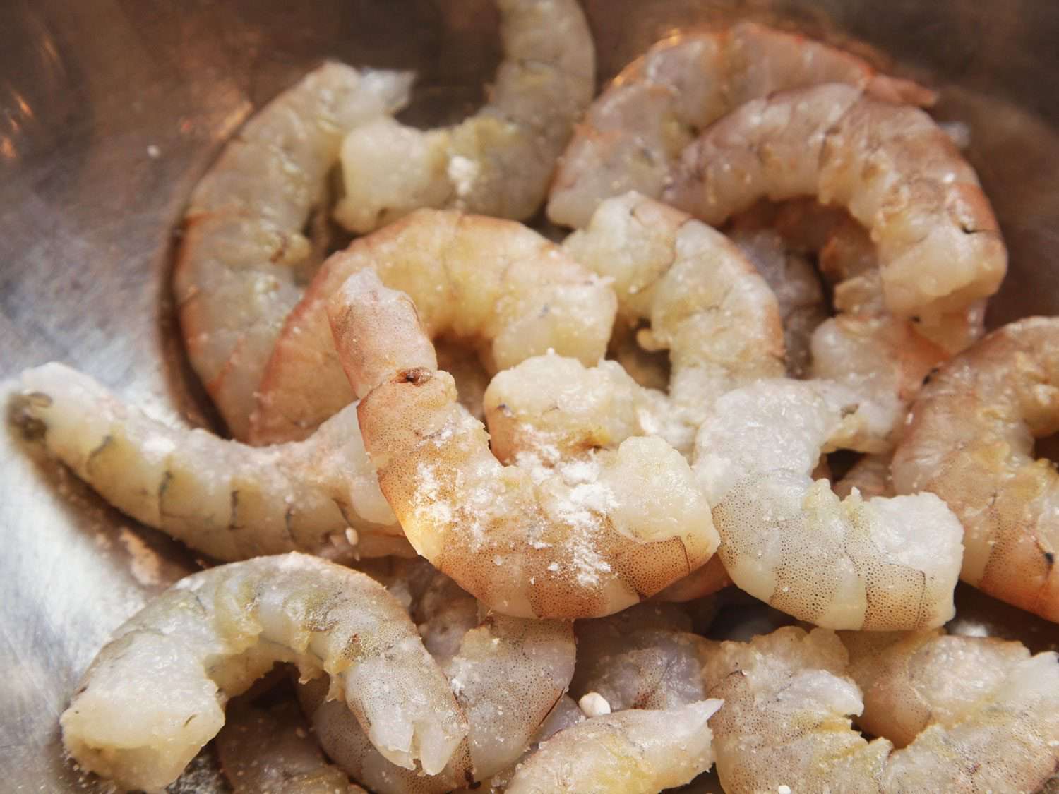Shelled and tailed shrimp in a bowl with sprinkling of baking soda on top.
