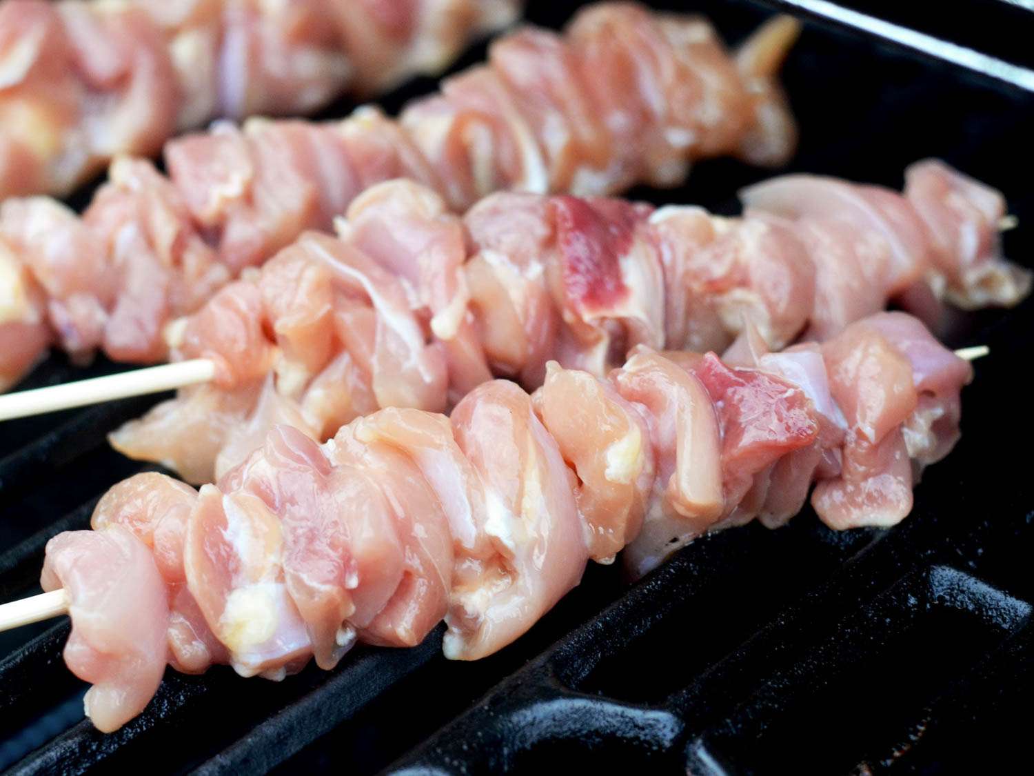 Marinated and skewered chicken is placed on the grill.