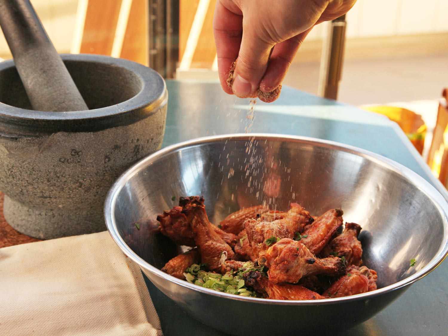 Toasted ground numbing spices being sprinkled over a bowl of crispy chicken wings and scallions.