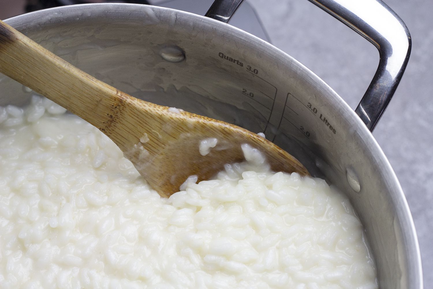 A zoomed in shot of a wooden spoon stirring risotto.