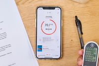 Smartphone displaying the Breville Joule Turbo Sous Vide Machine app interface, surrounded by a pen, paper, and a digital thermometer on a wooden surface