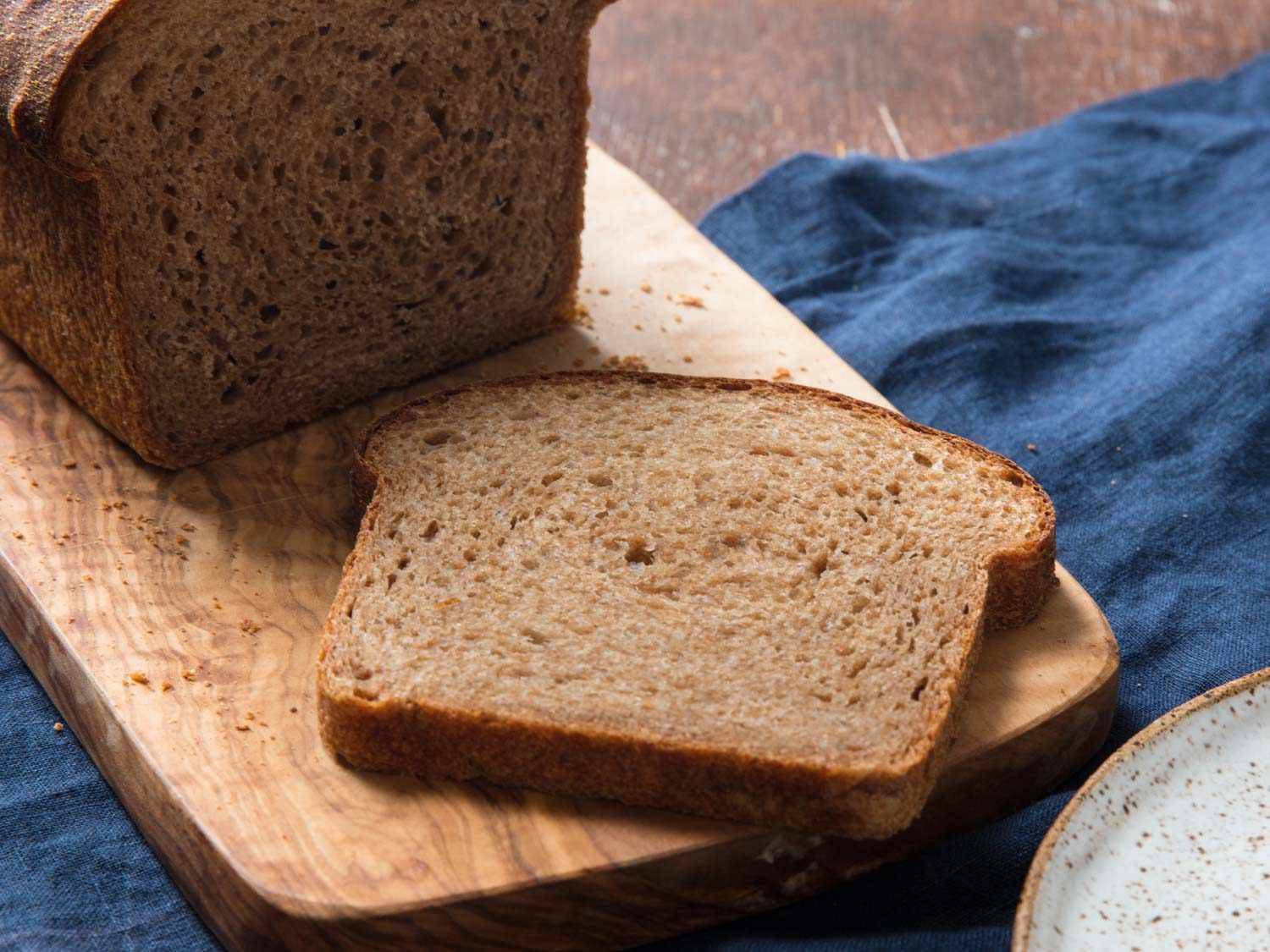A 100% whole wheat sandwich loaf, with a slice on a serving board. 